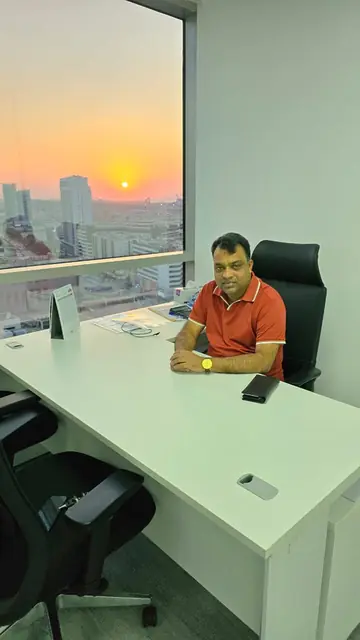 Abdul Kader Chowdhury at an office desk by the window at sunset